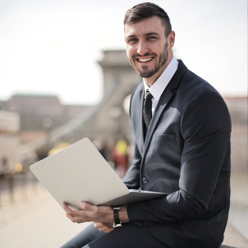 man in black suit jacket holding silver laptop computer